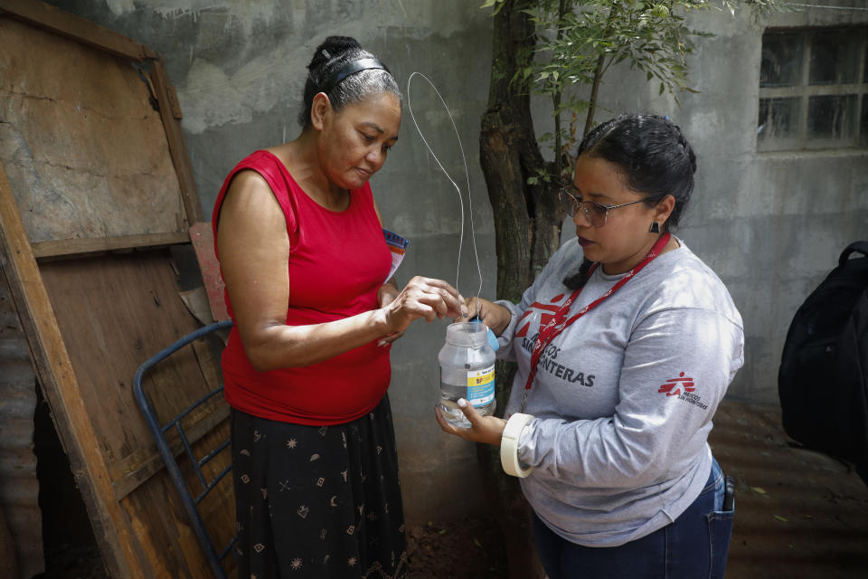 Martha Ocampo vierte una cápsula con huevos de mosquito en un jarro con agua siguiendo las instrucciones de una voluntaria de Médico Sin Fronteras, dentro de un programa para evitar la propagación del dengue, en Tegucigalpa, Honduras, el 23 de agosto de 2023. En lugar de eliminar los mosquitos, el programa incentiva la liberación de otros infectados con una bacteria llamada Wolbachia, que bloquea la propagación del dengue. (AP Foto/Elmer Martínez)