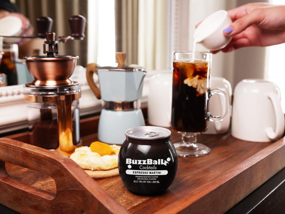 A wooden tray holding a BuzzBallz espresso martini and coffee accessories