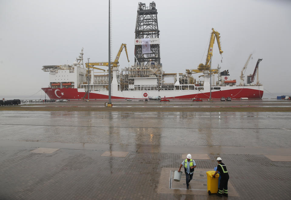 Port workers clean the dock area backdropped by the drilling ship 'Yavuz' scheduled to be dispatched to the Mediterranean, at the port of Dilovasi, outside Istanbul, Thursday, June 20, 2019. Turkish officials say the drillship Yavuz will be dispatched to an area off Cyprus to drill for gas. Another drillship, the Fatih, is now drilling off Cyprus' west coast at a distance of approximately 40 miles in waters where the east Mediterranean island nation has exclusive economic rights. The Cyprus government says Turkey's actions contravene international law and violate Cypriot sovereign rights. (AP Photo/Lefteris Pitarakis)
