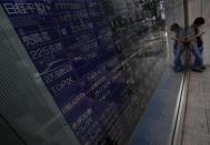 A pedestrian looks at his mobile phone stands in front of an electronic board showing various stock prices outside a brokerage in Tokyo, Japan, September 4, 2015. REUTERS/Yuya Shino