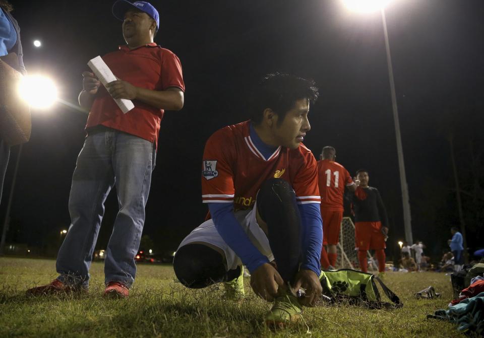 Pedro Chilel, 21, abandoned by his parents in Guatemala before he traveled alone to the United States at age 17, ties his shoes before his Maya Chapin soccer league game Wednesday, April 17, 2019, in Phoenix. As is common in Guatemalan indigenous communities ravaged by alcoholism, Chilel was abandoned by his parents before traveling to the U.S. alone at 17. He now lives in Phoenix, where he has permanent U.S. residency, a landscaping job and a sense of community he lacked in his village of Mirador. Antonio Velasquez, pastor and director of the soccer league, stands behind Chilel. (AP Photo/Ross D. Franklin)