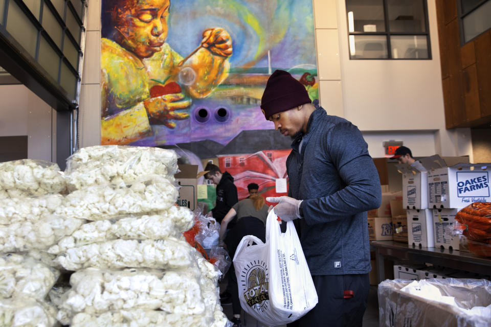 In this March 25, 2020, photo, entrepreneur and volunteer JoJo Houston, 26, of Guul Monstru Pathways Inc, helps to pack cauliflower and other fresh produce into bags for grocery distribution at Martha's Table headquarters in southeast Washington. Neighborhood volunteers such as Houston are the tip of the spear for a grassroots community effort to keep Washington's most vulnerable neighborhoods fed during the unprecedented coronavirus crisis which has nearly shut down the American economy. (AP Photo/Jacquelyn Martin)