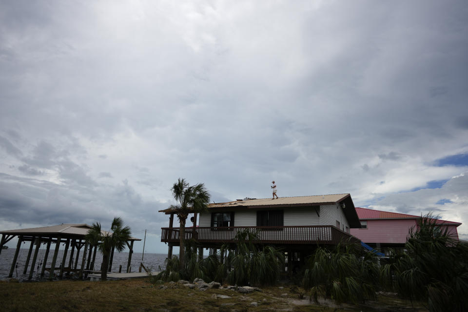 A person inspects damage to the roof of a waterfront home on stilts, in Horseshoe Beach, Fla., Thursday, Aug. 31, 2023, one day after the passage of Hurricane Idalia. (AP Photo/Rebecca Blackwell)