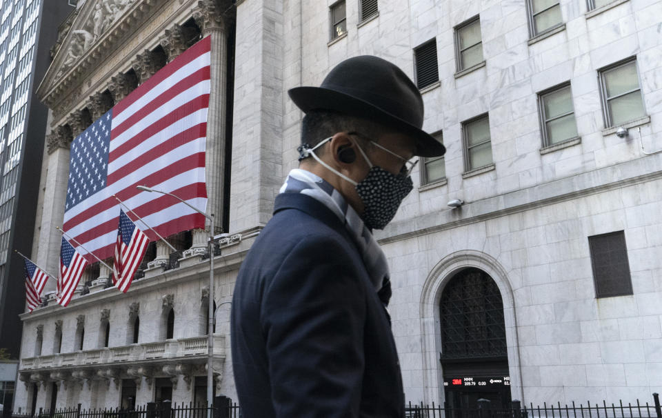 FILE - In this Nov. 16, 2020 file photo a man wearing a mask passes the New York Stock Exchange in New York.  Time stood still for most of the world in 2020, as lockdown life had every day bleeding into the next. But for Wall Street, it’s been a year locked in at super fast-forward. The stock market tumbled through years’ worth of losses in just over a month this spring, only to turn around and pack an entire bull market’s worth of gains into less than nine months.  (AP Photo/Mark Lennihan, File)