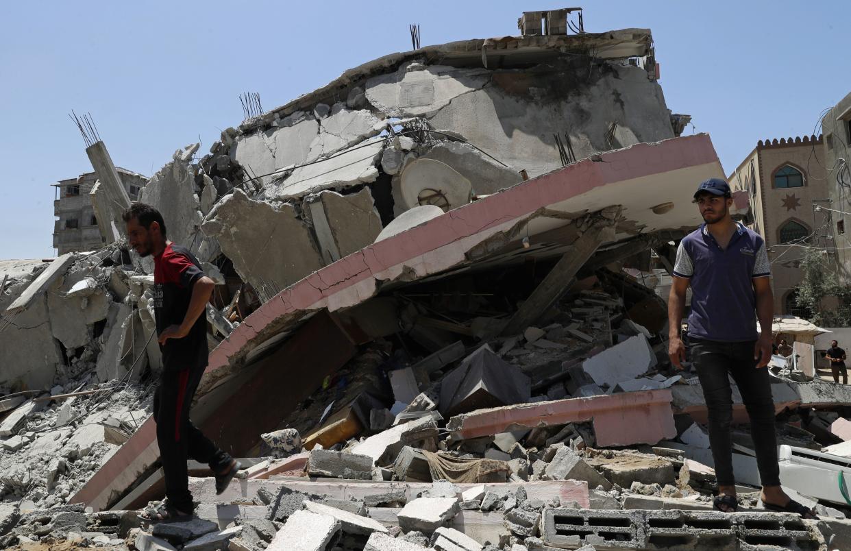 People walk amid the rubble of a destroyed residential building which was hit by Israeli airstrikes, in Gaza City, Wednesday, May 12, 2021. (AP Photo/Adel Hana)