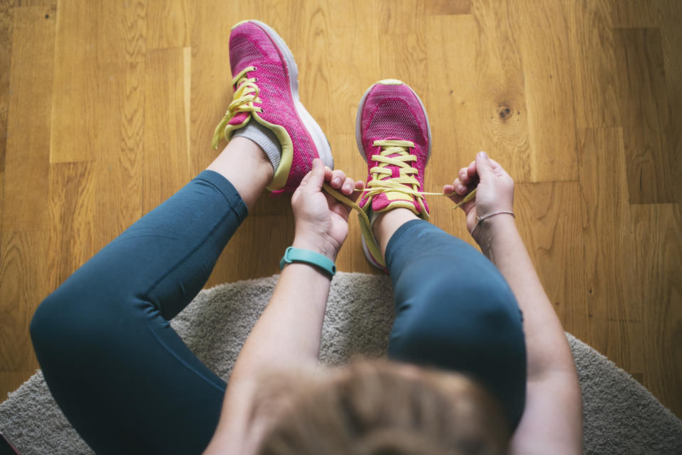 A person lacing up pink and yellow running shoes, preparing to exercise. (Photo via Getty Images)