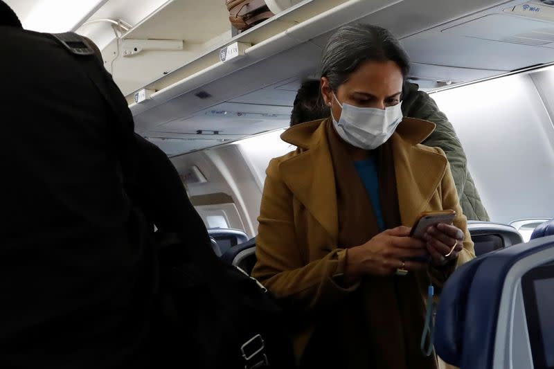 A woman in a face mask checks her phone after landing on a flight from San Francisco to New York City, after further cases of coronavirus were confirmed in New York, at JFK International Airport in New York