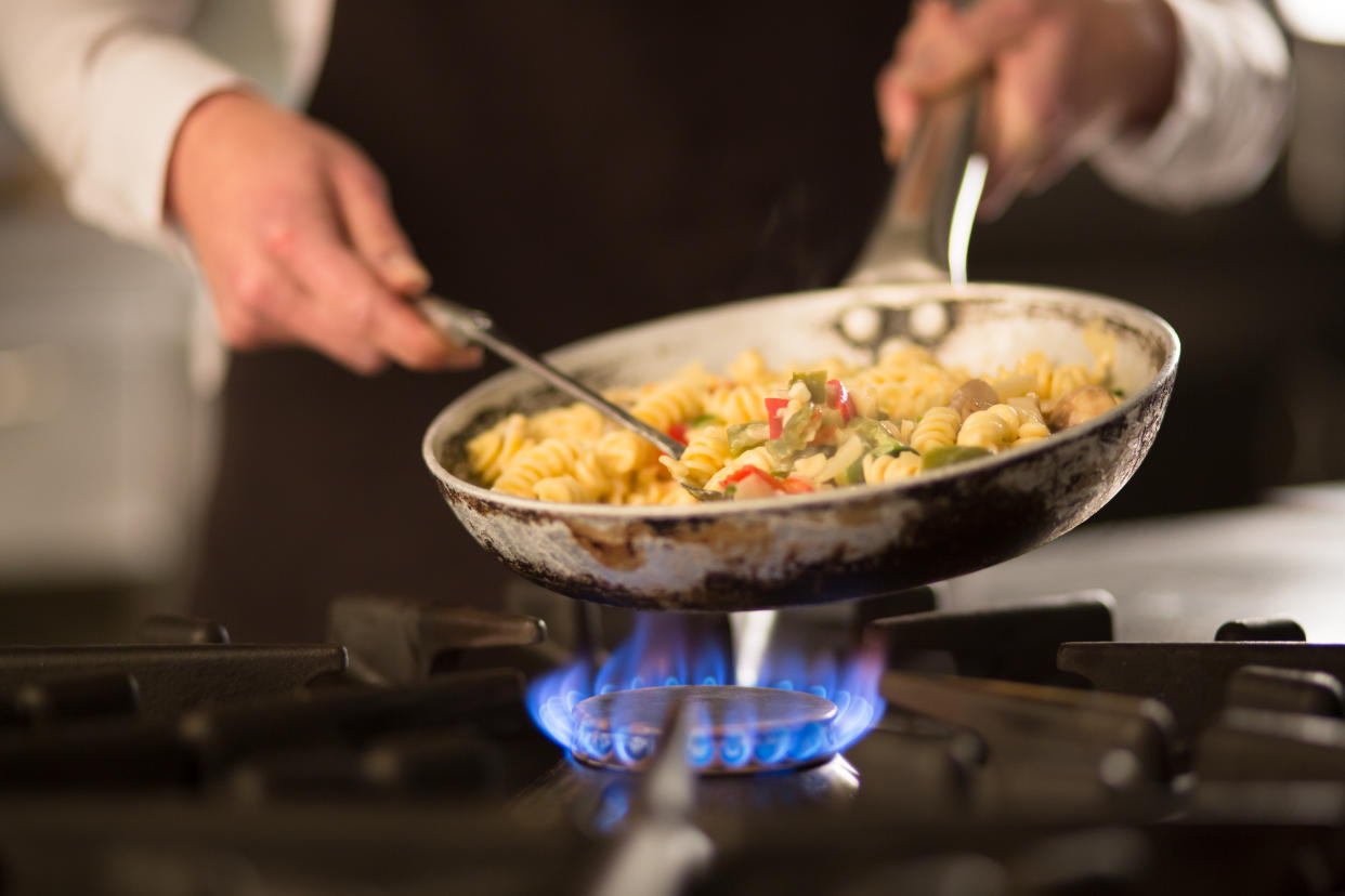 A pan of pasta is held by over a gas flame on high.