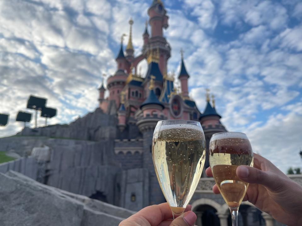 two people cheersing champagne flutes in front of the castle at disneyland paris