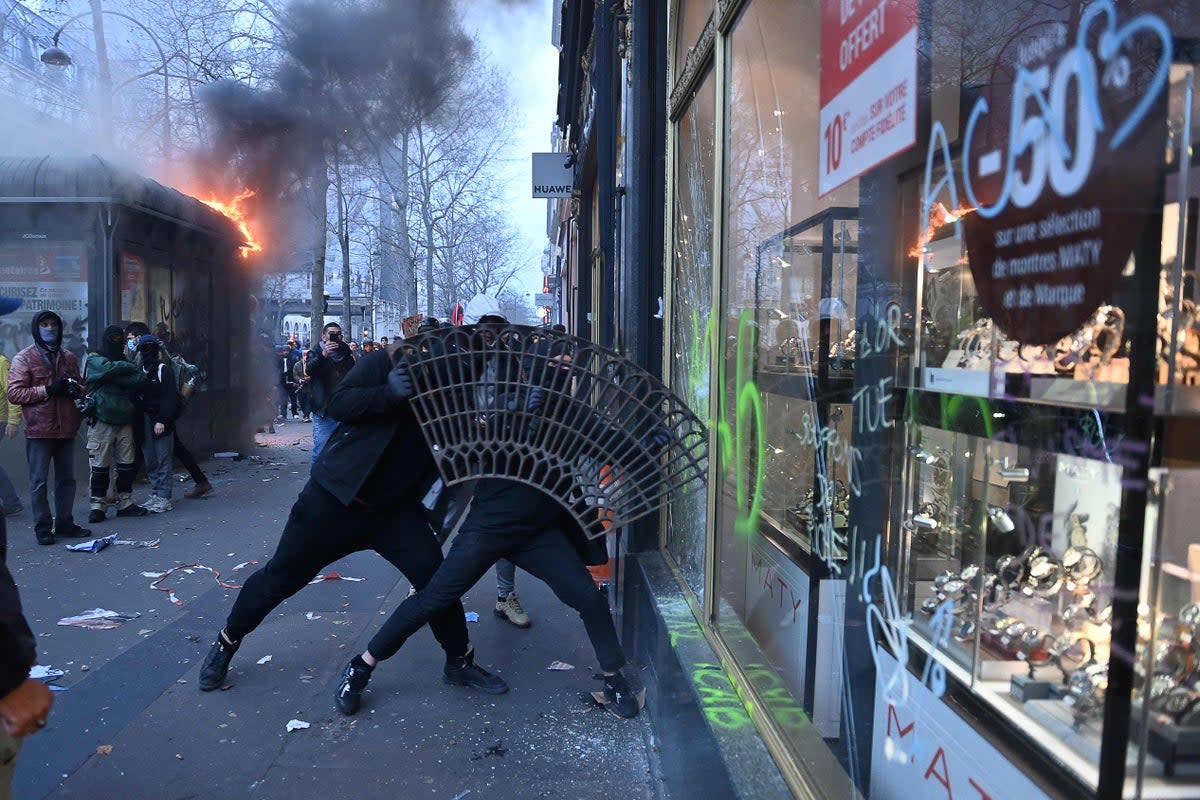 Protesters use a sidewalk tree grid to break the window of a shop on the sidelines of a demonstration as part of a national day of strikes and protests, a week after the French government pushed a pensions reform through parliament without a vote, using the article 49.3 of the constitution, in Paris (AFP via Getty Images)