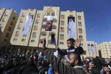 Posters depicting Qatar's former Emir Sheikh Hamad bin Khalifa al-Thani (R) and Emir of Qatar Tamim bin Hamad al-Thani (L) are seen on a building as a Palestinian man holding his son waves during the opening ceremony of Qatari-funded construction project "Hamad City", in Khan Younis in the southern Gaza Strip January 16, 2016. REUTERS/Ibraheem Abu Mustafa