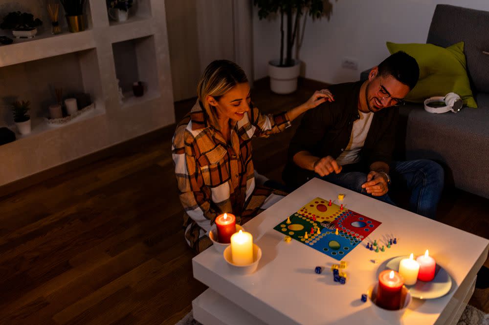 During an energetic crisis, a man and woman are playing a ludo game in the dark with lit candles.