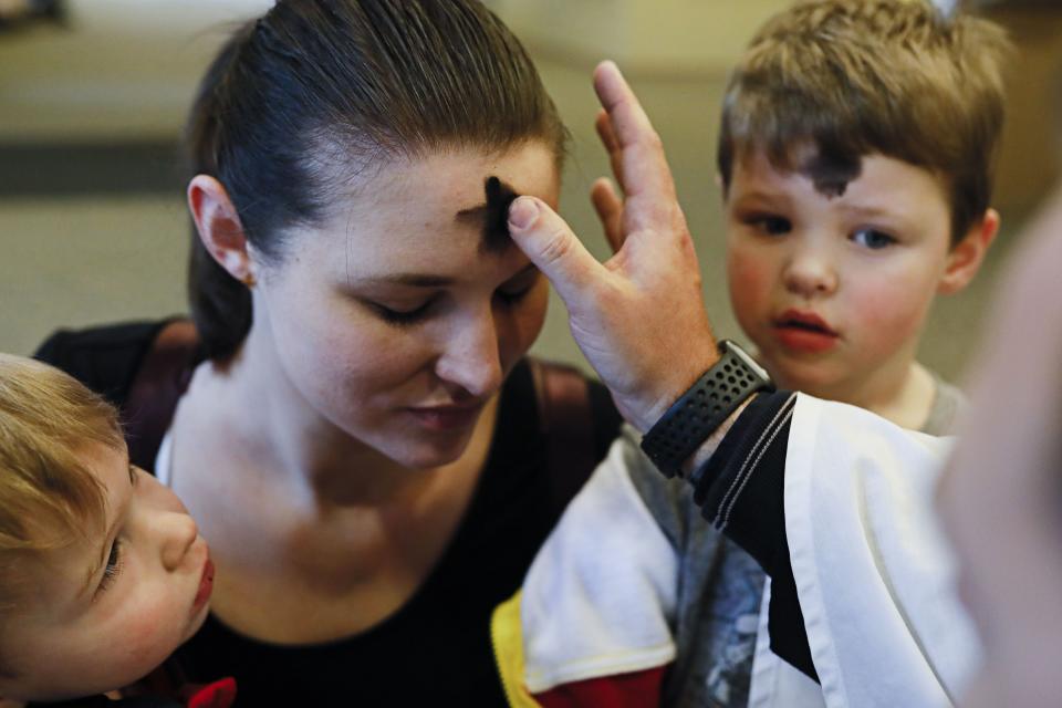 Stacey Berling, center, of Grove City, kneels with her sons, Harrison, 2, left, and Finneus, 4, right, as she receives ashes from Deacon Andrew Ames Fuller during an Ash Wednesday service as part of "Ashes To Go" on Wednesday, February 26, 2020 at Upper Arlington Lutheran Church Mill Run Campus in Hilliard, Ohio. Worshippers were able to come to the church and either stay in their car or come inside the building lobby to receive their ashes in lieu of a formal mass or service. Ash Wednesday marks the beginning of the Christian season of Lent.