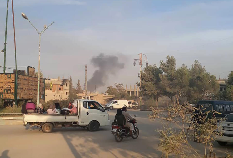 In this photo provided by Rojava Media Center, a pro-Kurdish media group, Syrians flee as smoke rises from shelling by Turkish forces, in Ras al Ayn, northeast Syria, Wednesday, Oct. 9, 2019. Turkish President Recep Tayyip Erdogan announced Wednesday the start of a Turkish military operation against Kurdish fighters in northeastern Syria. (Rojava Media Center via AP)