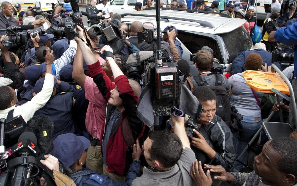 Journalist swamp Oscar Pistorius, as escorted out by his private security and police officers at the high court at the end second day of his trial in Pretoria, South Africa, Tuesday, March 4 2014. Oscar Pistorius is charged with murder for the shooting death of his girlfriend, Reeva Steenkamp, on Valentines Day in 2013. (AP Photo/Themba Hadebe)