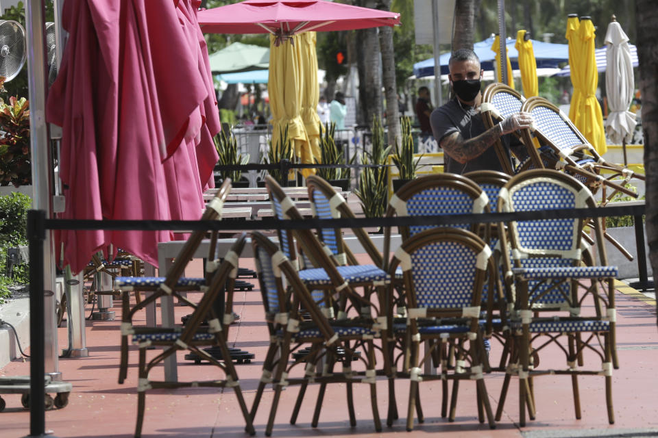 An employee at the Clevelander bar and restaurant on Ocean Drive stacks chairs as they have shut down due to public health concerns caused by COVID-19 during the coronavirus pandemic, Monday, July 13, 2020, in Miami Beach, Fla. (AP Photo/Lynne Sladky)