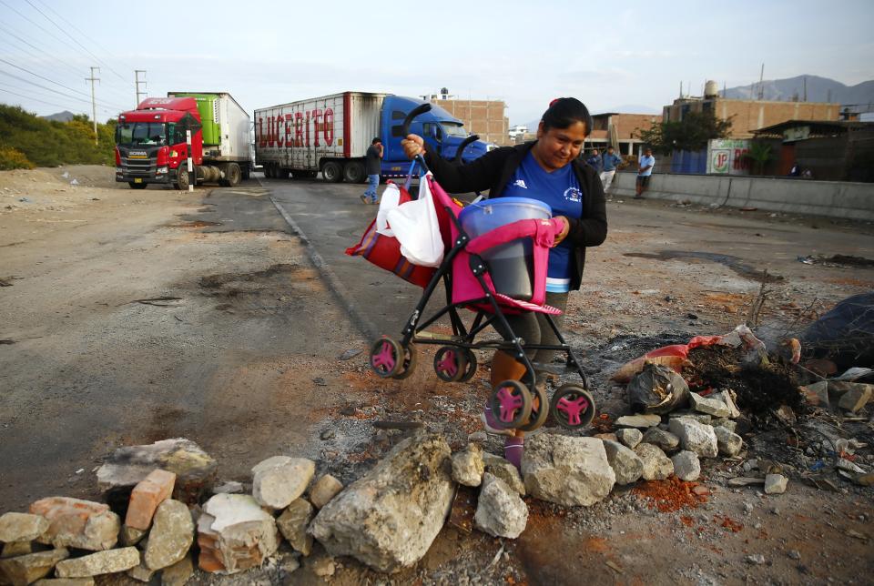 A "chicha" vendor lifts a baby carrier, carrying a bucket of the ice-cold beverage, over a barricade blocking the Pan-American North Highway placed by supporters of ousted Peruvian President Pedro Castillo protesting his detention in Viru, Peru, Thursday, Dec.15, 2022. Peru's new government declared a 30-day national emergency on Wednesday amid violent protests following Castillo's ouster, suspending the rights of "personal security and freedom" across the Andean nation. (AP Photo/Hugo Curotto)