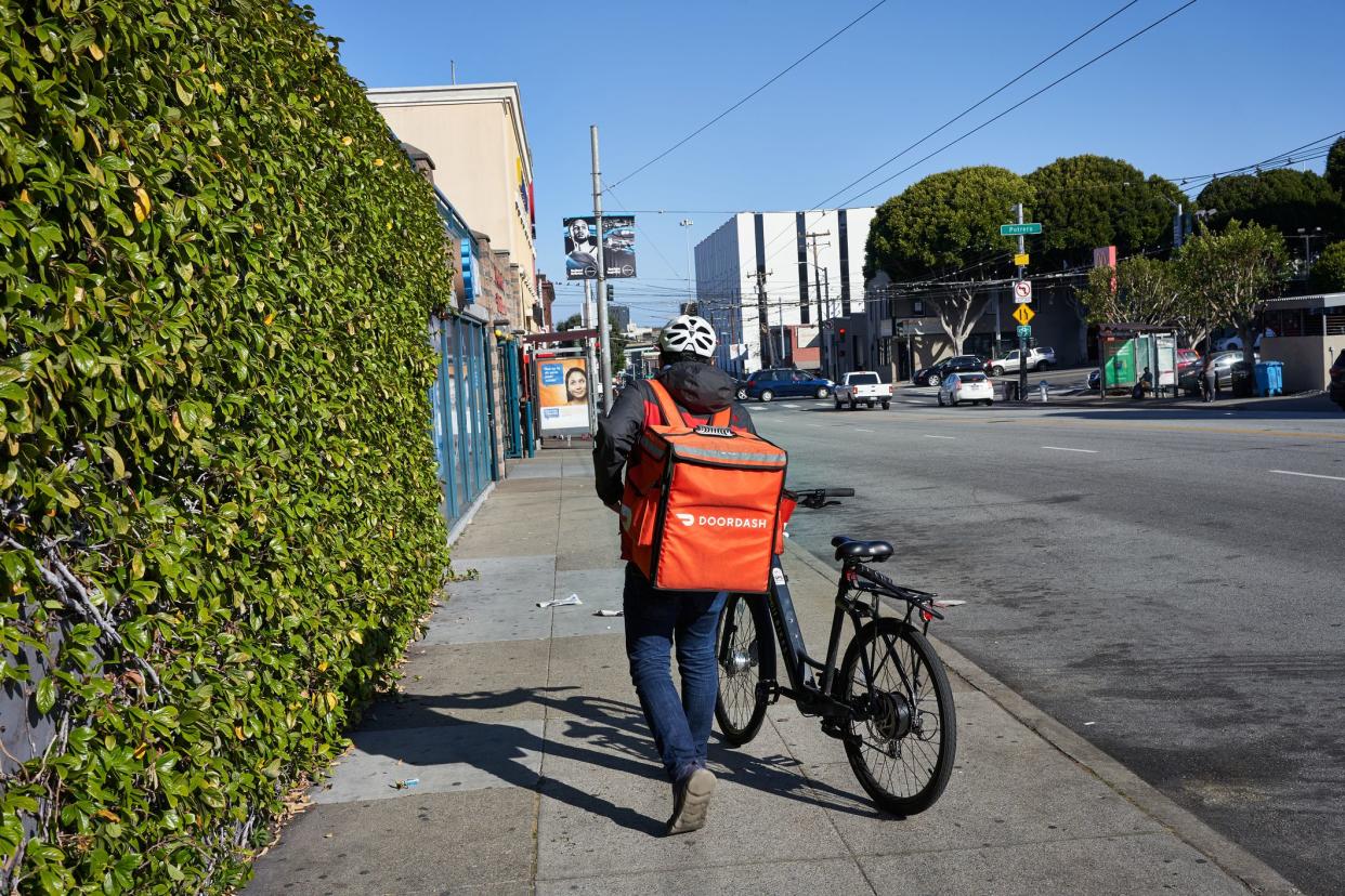 San Francisco, CA, USA - Feb 8, 2020: A DoorDash delivery worker walks his bike along the road in the Mission neighborhood of San Francisco, California.