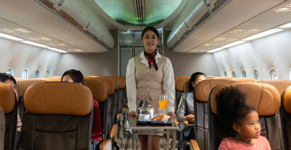 Flight attendant serving passengers on a plane, with a food cart