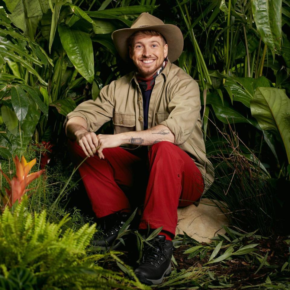 i'm a celebrity 2023, sam thompson, sitting on a rock in his jungle outfit