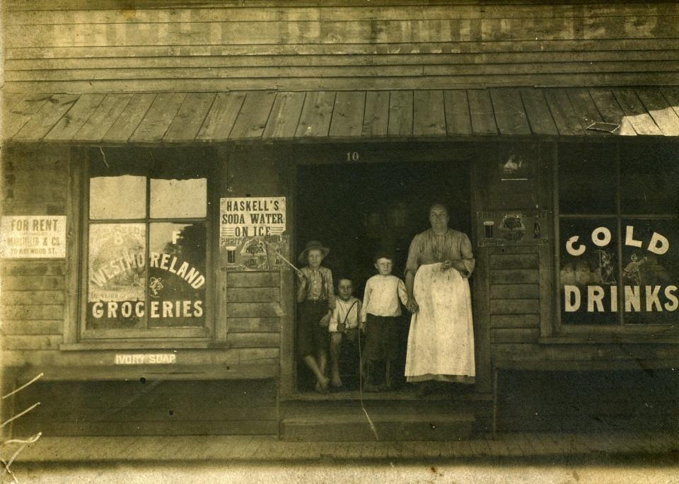 Lillian Moore Westmoreland poses in the doorway of Westmoreland Grocery at 10 Roberts Street, April 1902.  Left to right are Ralph Robinson, a family friend; and two sons, Ray and Walter Westmoreland.