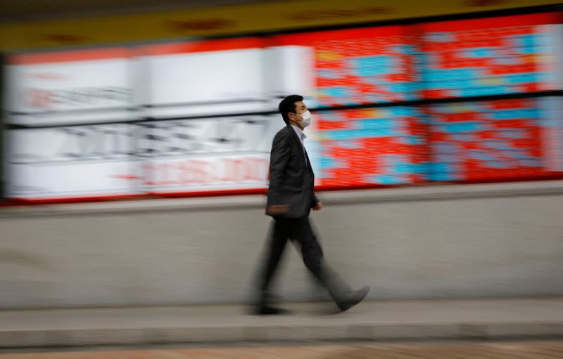 A man wearing a protective face mask, following the coronavirus disease (COVID-19) outbreak, walks in front of a stock quotation board outside a brokerage in Tokyo