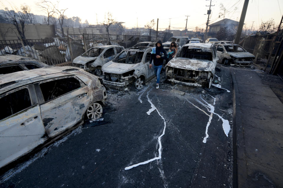 Locals walk among burnt cars after a forest fire reached the neighborhood of Villa Independencia in Vina del Mar, Chile, Saturday, Feb. 3, 2024. (AP Photo/ Esteban Felix)