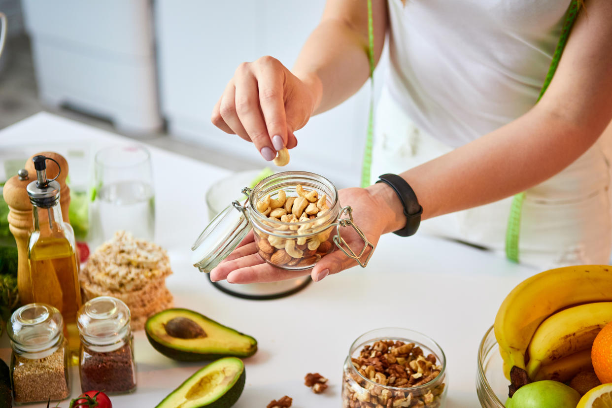 Young happy woman eating different nuts (cashew, hazelnut, almond) in modern kitchen. Healthy food and Dieting concept. Loosing Weight