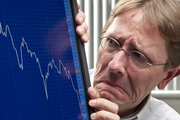 A visibly worried stock trader looking at a plunging chart on his computer monitor.