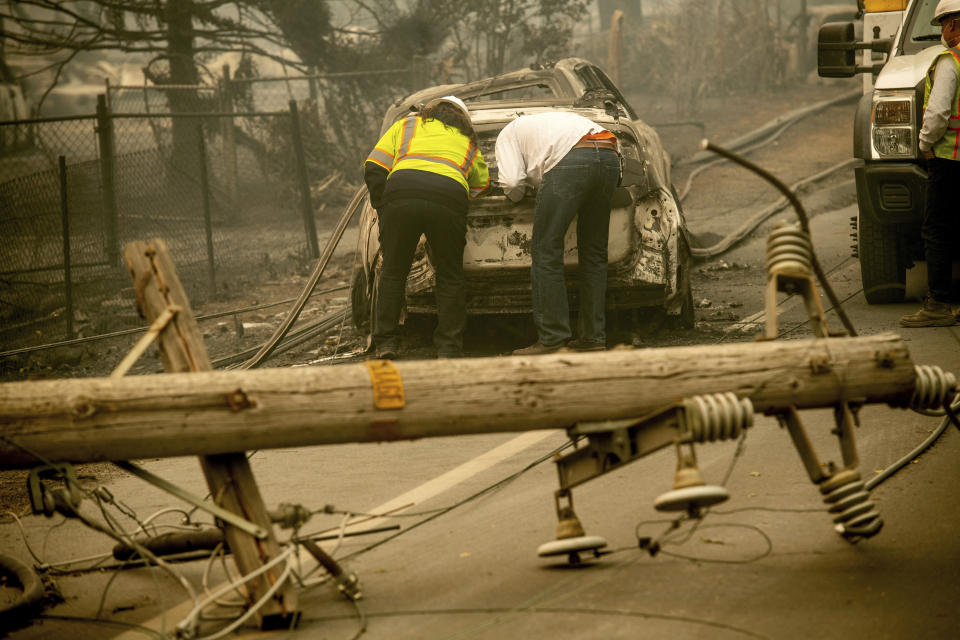 FILE - In this Nov. 10, 2018 file photo, with a downed power utility pole in the foreground, Eric England, right, searches through a friend's vehicle after the wildfire burned through Paradise, Calif. Pacific Gas & Electric has agreed to pay $11 billion to a group of insurance companies representing most of the claims from Northern California wildfires in 2017 and 2018 as the company tries to emerge from bankruptcy, the utility announced Friday, Sept. 13, 2019. (AP Photo/Noah Berger, File)