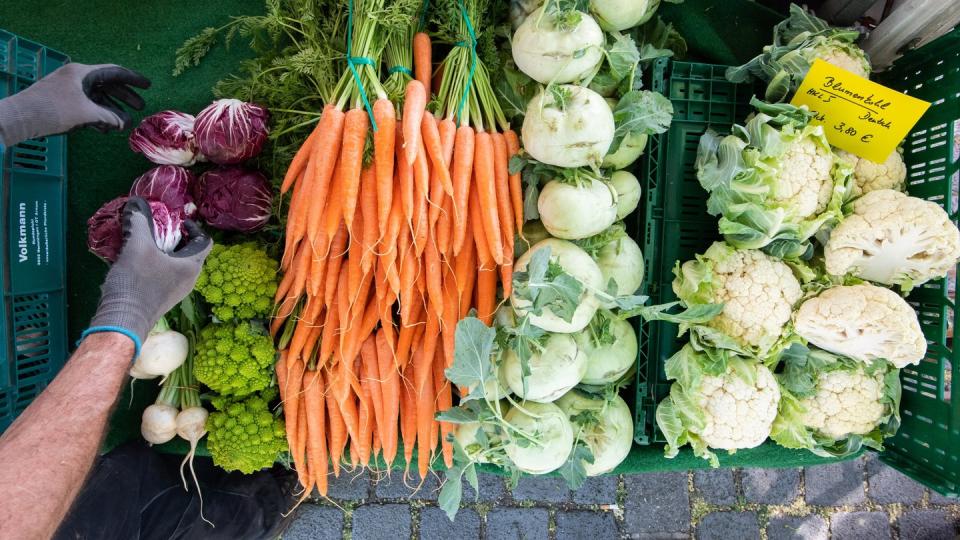 Ein Händler sortiert an seinem Verkaufsstand auf einem Wochenmarkt frisches Gemüse.