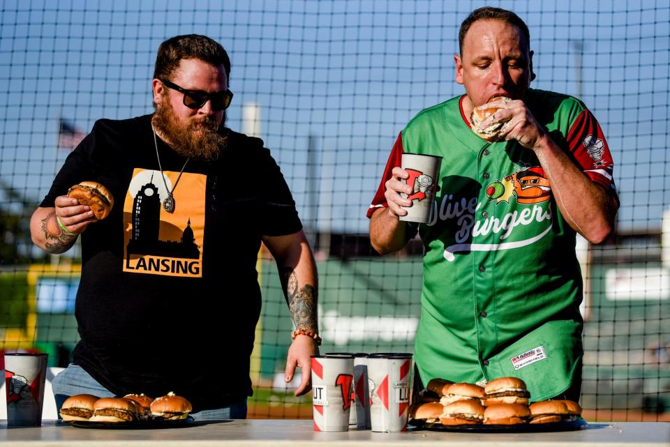 Ben Murphy, of Lansing, left, competes with Nathan's Hot Dog Eating champion Joey Chestnut in a 5-minute olive burger eating contest before the Lugnuts game against the TinCaps on Thursday, Aug. 10, 2023, at Jackson Field in Lansing. Murphy ate 9 and a half in 10 minutes during the Lansing Olive Burger Festival last year. Chestnut set a record with 13 olive burgers eaten in 5 minutes, beating Murphy's 5.