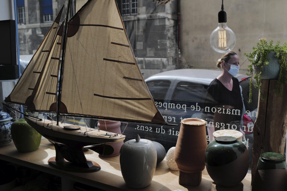 Funeral urns are displayed in the shop window of Paris undertaker Franck Vasseur of L'autre rive funeral directors, as a woman wearing protective mask walks by outside in the street, prior to a funeral ceremony at Pere Lachaise cemetery in Paris, Friday, April 24, 2020. Vasseur says that dealing with a flood of coronavirus victims' bodies since March has turned his life into an infernal, head-spinning procession of death and that he feels robbed of his purpose by being unable to comfort families who cannot accompany bodies for cremation or gather in large numbers for funerals. (AP Photo/Francois Mori)