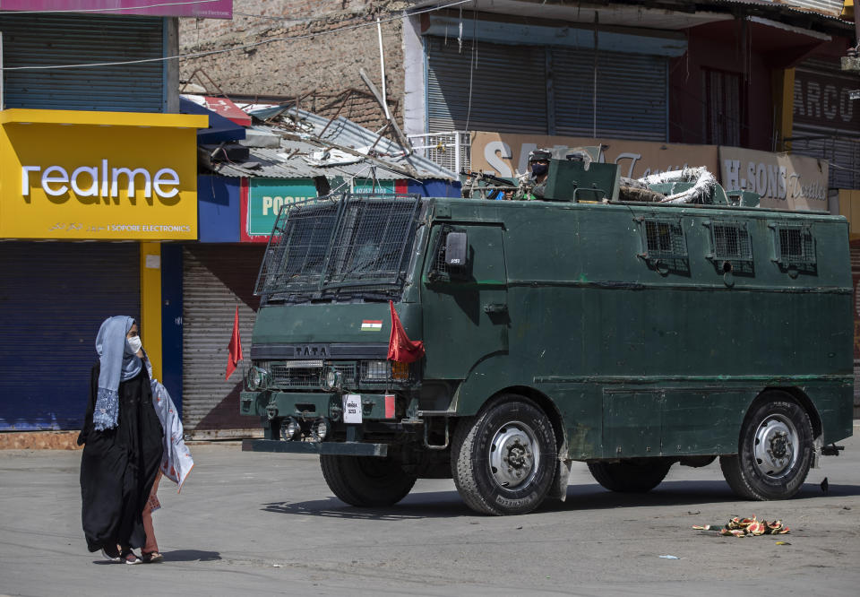 Kashmiri women walk past soldiers guarding near the site of a shootout at Sopore, 55 kilometers (34 miles) north of Srinagar, Indian controlled Kashmir, Saturday, June 12, 2021. Two civilians and two police officials were killed in an armed clash in Indian-controlled Kashmir on Saturday, police said, triggering anti-India protests who accused the police of targeting the civilians. (AP Photo/Mukhtar Khan)