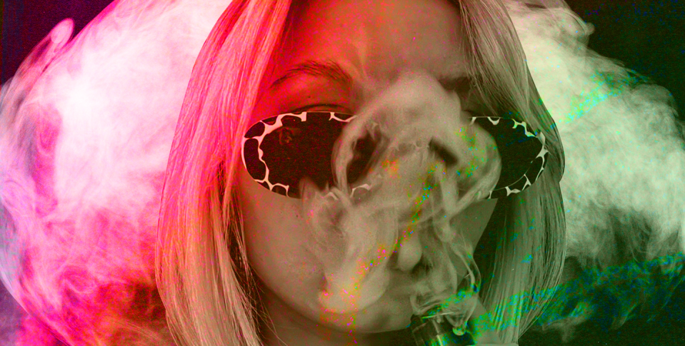 a woman in sunglasses, shrouded in red and green smoke as she vapes