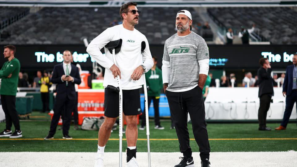 Aaron Rodgers of the New York Jets stands on the field holding crutches prior in October, a few weeks after his Achilles injury. - Kevin Sabitus/Getty Images