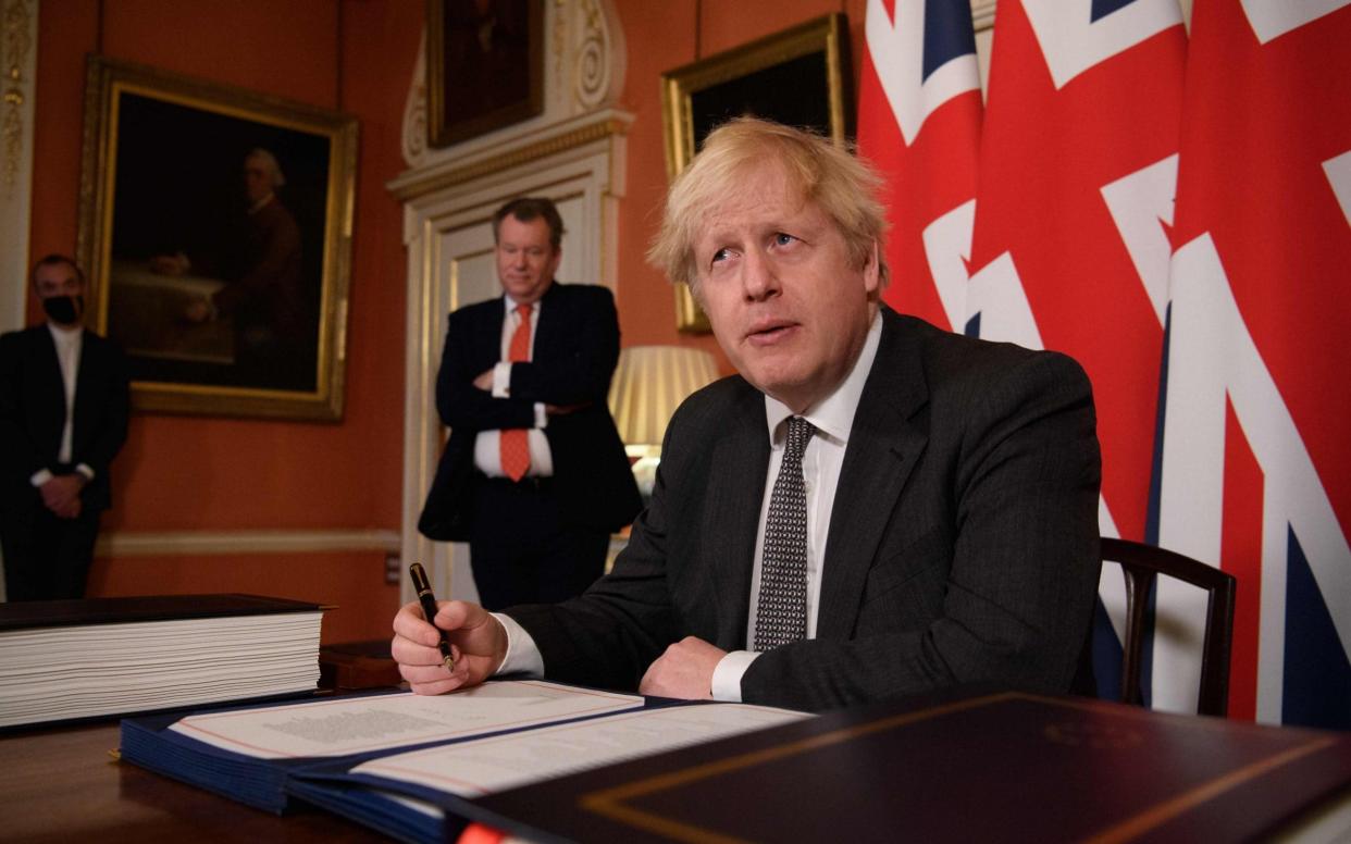 Boris Johnson signs the Trade and Cooperation Agreement between the UK and the EU, as David Frost looks on - LEON NEAL/AFP