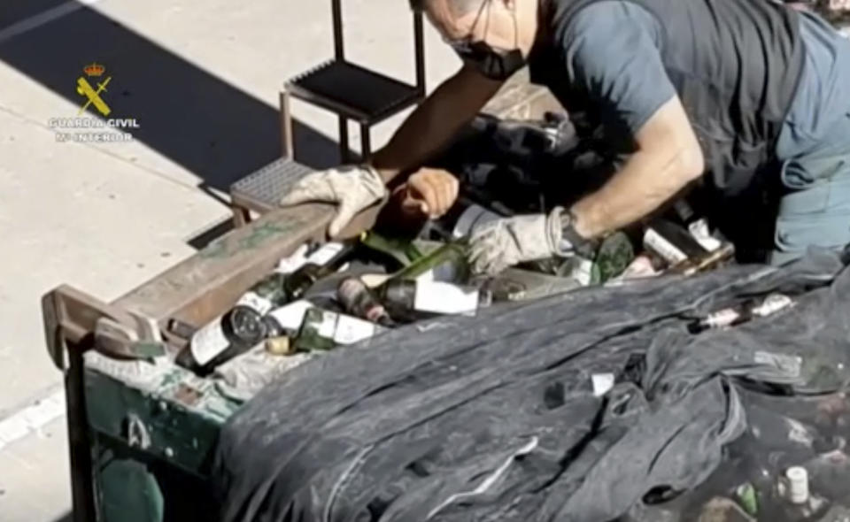 In this image taken from video made available by the Guardia Civil, an officer of the Guardia Civil helps a man out from under glass bottles in a container in Melilla, Spain, Friday Feb. 19, 2021. Spanish authorities say they have found and rescued 41 migrants who tried to reach continental Europe from North Africa in the past four days, some of them hiding inside a container of discarded glass bottles and a bag of toxic ash. (Guardia Civil via AP)