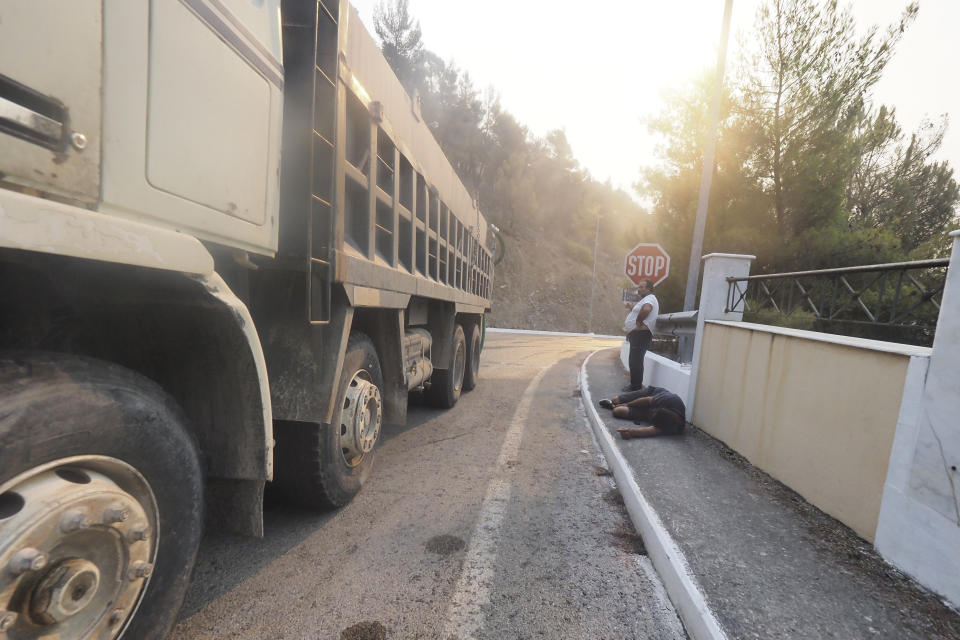 A man rests on the ground as another stands nearby in Limni village on the island of Evia, about 160 kilometers (100 miles) north of Athens, Greece, Saturday, Aug. 7, 2021. Wildfires rampaged through massive swathes of Greece's last remaining forests for yet another day Saturday, encroaching on inhabited areas and burning scores of homes, businesses and farmland. (AP Photo/Thodoris Nikolaou)