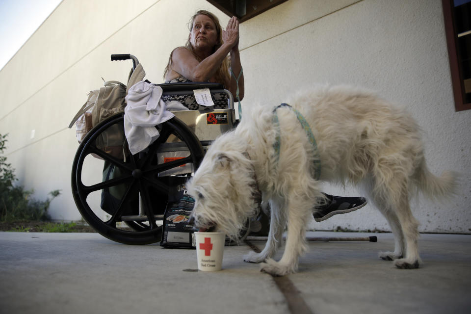 Mary, no last name given, sits on her wheelchair next to her dog Manny, outside of the gym at West Ranch High School after being evacuated from the Tick Fire Friday, Oct. 25, 2019, in Santa Clarita, Calif. (AP Photo/Marcio Jose Sanchez)