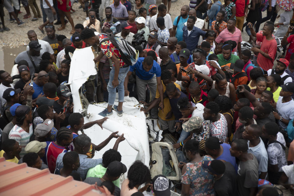 Onlookers mill around the wreckage of a small plane that crashed in the community of Carrefour, Port-au-Prince, Haiti, Wednesday, April 20, 2022. Police report that the plane was headed to the southern coastal city of Jacmel when it tried to land in Carrefour, and that at least 5 people died in the accident. (AP Photo/Odelyn Joseph)