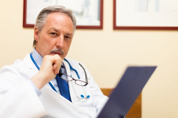 A doctor pondering what he's just read on a clipboard.