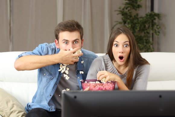 A young couple, excitedly eating popcorn in front of the TV.