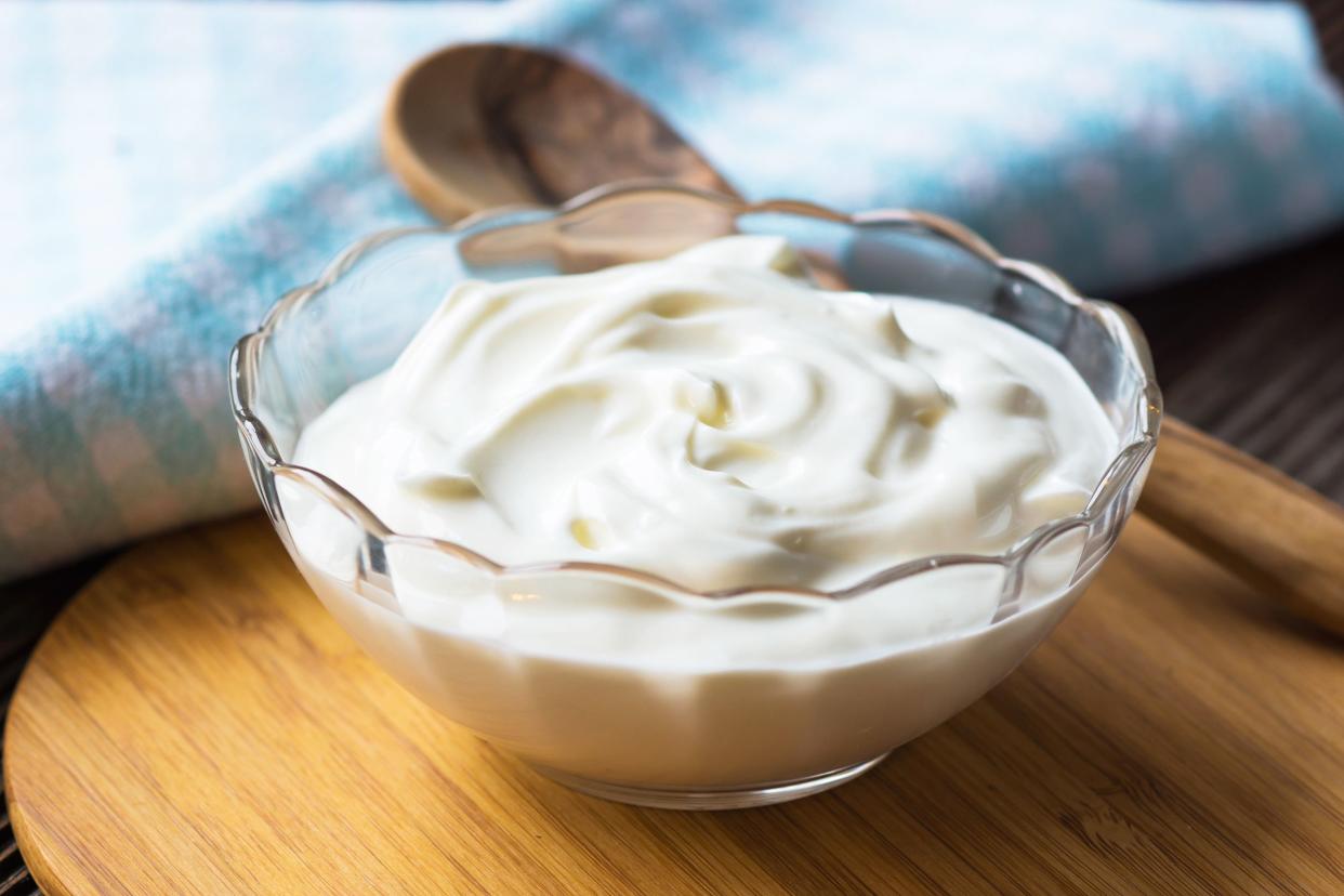 Greek yogurt in a decorative glass bowl, selective focus, with a wooden spoon, on a wooden serving plate with a light blue checked napkin