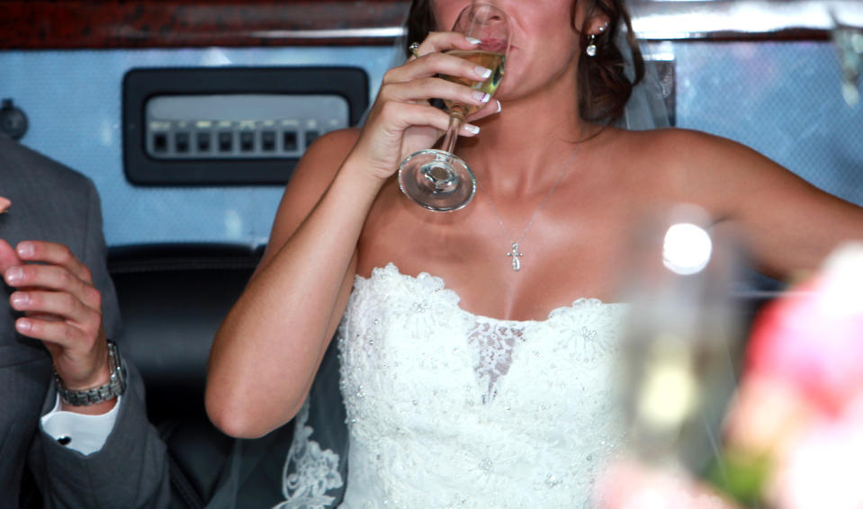 Bride in a lace strapless wedding gown sips champagne inside a vehicle