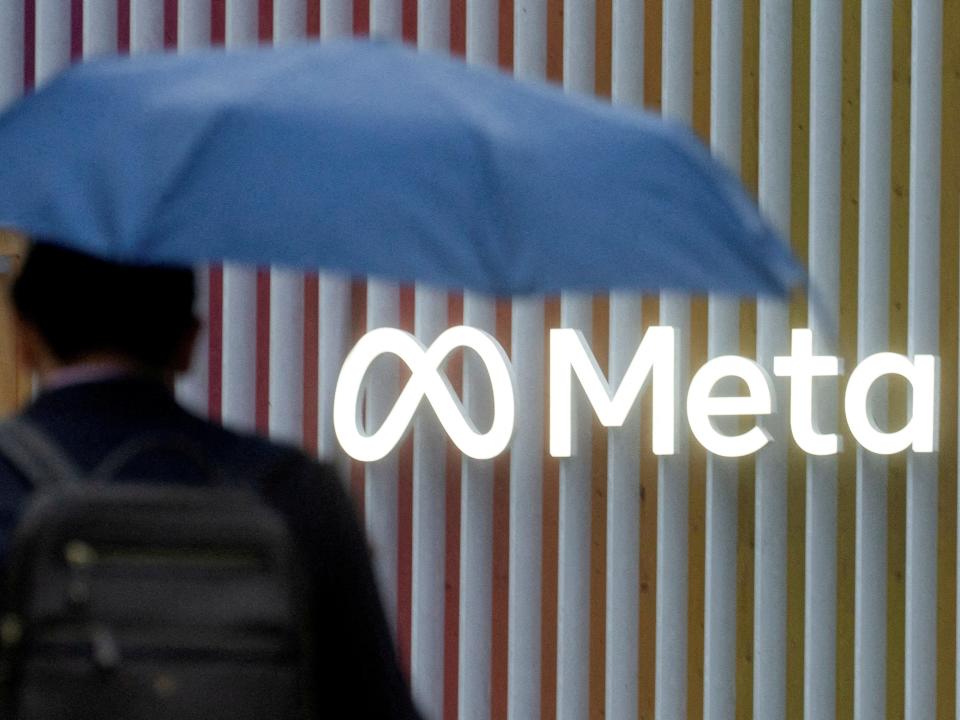 Man with blue umbrella with back against Meta logo.