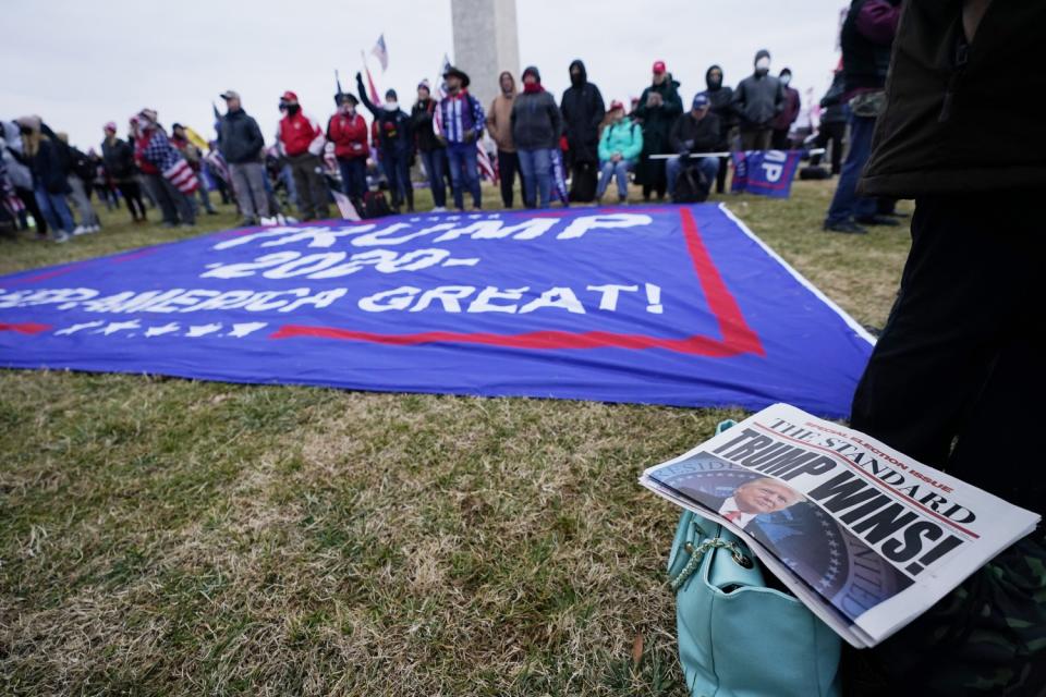 Trump supporters with a banner on the grass and a newspaper saying Trump Wins! gather in front of the Washington Monument.