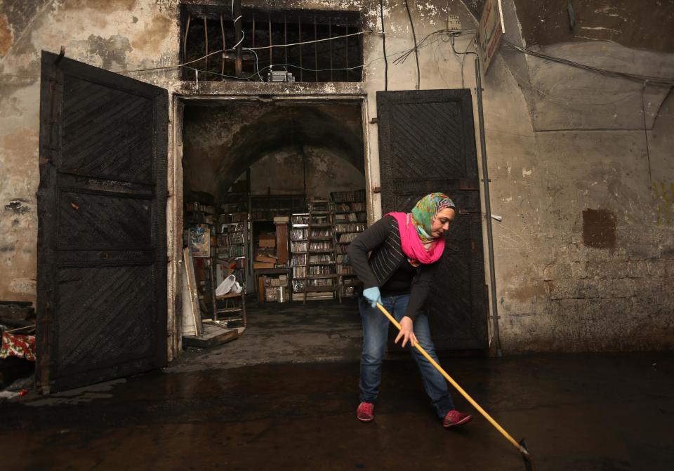 In this picture taken on Sunday, Jan. 5, 2014, a Lebanese activist cleans the ground in front the entrance of the Saeh (Tourist) Library which was set on fire by masked men, in the northern city of Tripoli, Lebanon. Books that were burnt in an arson attack targeting a crammed, chaotic and popular library in the northern Lebanese city of Tripoli have become the latest victim of the country's rising sectarian tensions.(AP Photo/Hussein Malla)