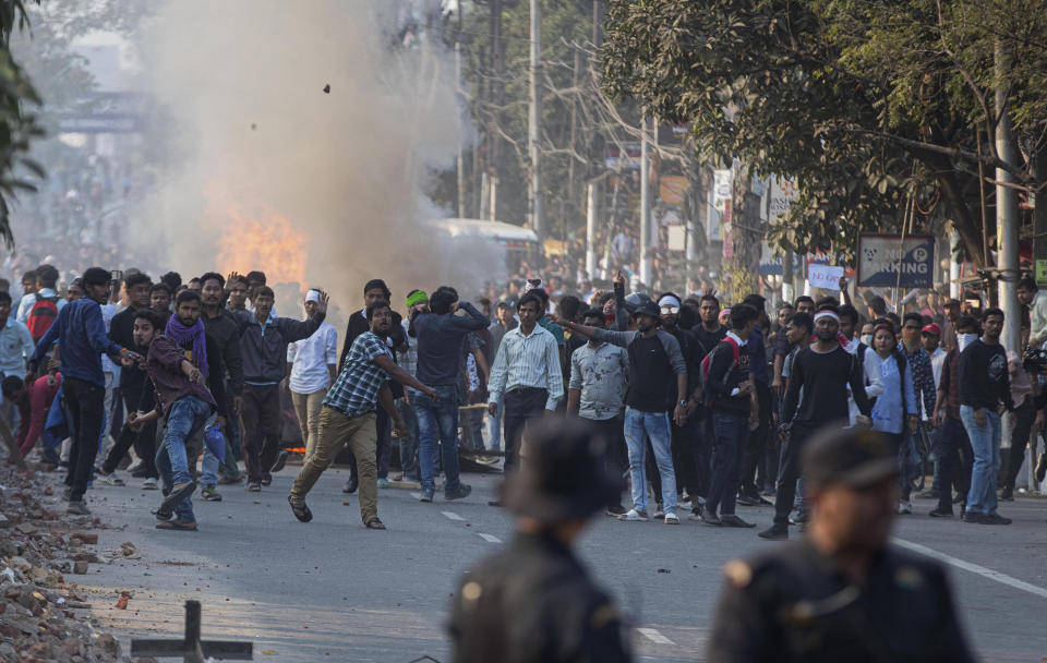 Protestors throw stones at security officers during a protest against the Citizenship Amendment Bill (CAB) in Gauhati, India, Wednesday, Dec. 11, 2019. Protesters burned tires and blocked highways and rail tracks in India's remote northeast for a second day Wednesday as the upper house of Parliament began debating legislation that would grant citizenship to persecuted Hindus and other religious minorities from Pakistan, Bangladesh and Afghanistan. (AP Photo/Anupam Nath)