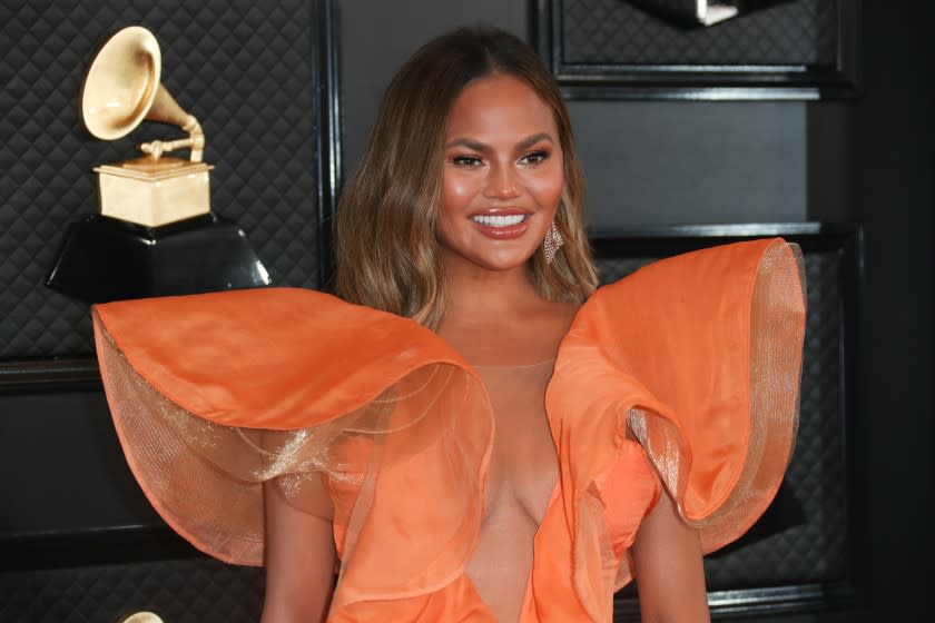 Chrissy Teigen smiling in a ruffled orange dress